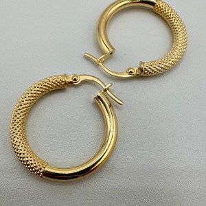 May include: A pair of gold hoop earrings with a textured design. The earrings have a hinged closure.