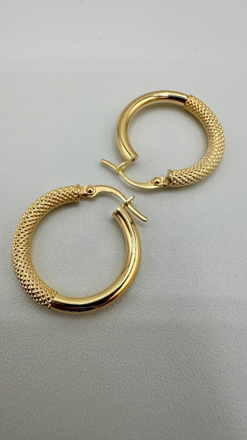 May include: A pair of gold hoop earrings with a textured design. The earrings have a hinged closure.