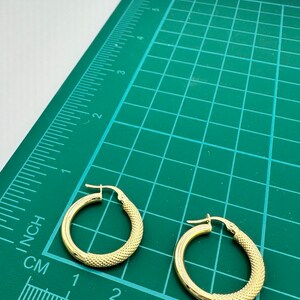 May include: Two gold hoop earrings with a textured surface. The earrings are approximately 2 inches in diameter and are shown on a green cutting mat with a ruler.