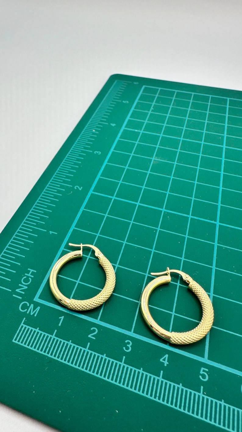 May include: Two gold hoop earrings with a textured surface. The earrings are approximately 2 inches in diameter and are shown on a green cutting mat with a ruler.
