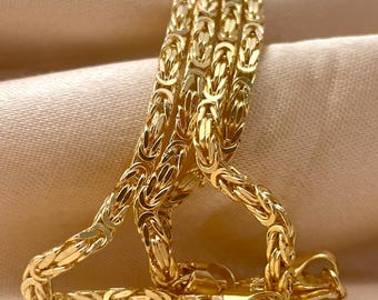 May include: A gold Byzantine chain necklace featuring a complex, woven link pattern with a polished, reflective finish. The necklace includes a secure lobster claw clasp at the end, showcasing a continuous, intricate design throughout the entire length.