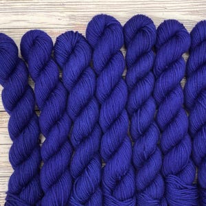 May include: Close-up of seven skeins of vibrant blue yarn, arranged side by side. The yarn is tightly wound, creating a textured surface. The background is a light-colored wooden surface.