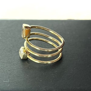 Puede incluir: Un anillo de oro con tres bandas y dos piedras preciosas transparentes. El anillo est&aacute; sobre una superficie negra.