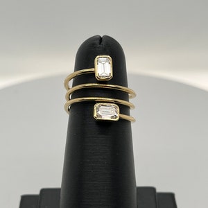 Puede incluir: Un anillo de oro con dos diamantes de talla esmeralda engastados en una banda en espiral.