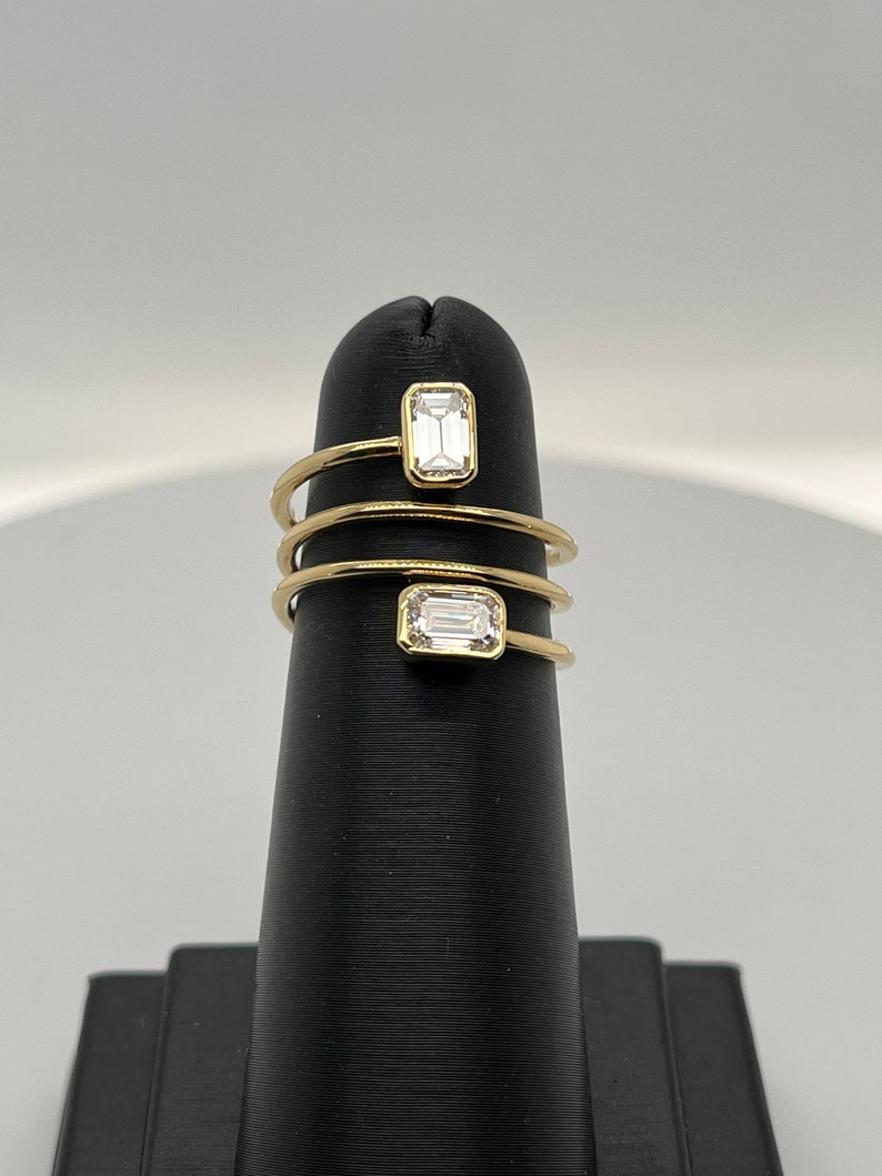 Puede incluir: Un anillo de oro con dos diamantes de talla esmeralda engastados en una banda en espiral.