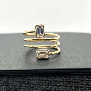 Puede incluir: Un anillo de oro con un dise&ntilde;o en espiral y dos diamantes de talla esmeralda.