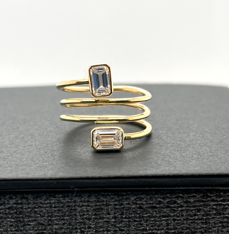 Puede incluir: Un anillo de oro con un dise&ntilde;o en espiral y dos diamantes de talla esmeralda.