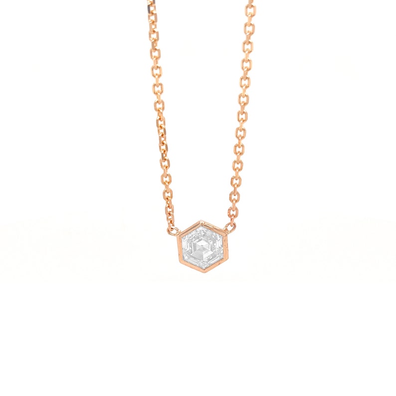 May include: A rose gold chain necklace featuring a single hexagonal pendant. The pendant is set with a clear, faceted, hexagonal-shaped stone that reflects light, held securely within a thin rose gold metal frame attached to the delicate chain.