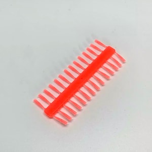 Può includere: Un pettine di plastica rosa brillante con una fila di denti piccoli e sottili. Il pettine è progettato per essere utilizzato con le extension per capelli.