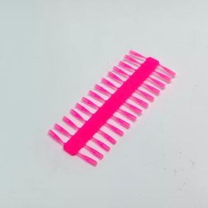 Può includere: Una striscia di plastica rosa con file di piccole setole appuntite in plastica rosa.