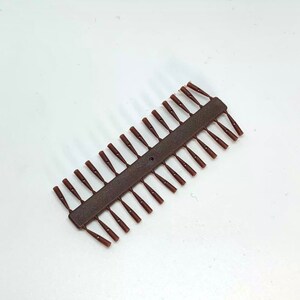 Può includere: Una spranga di plastica marrone con 28 piccoli pezzi di plastica marrone attaccati ad essa. I pezzi sono a forma di piccoli coni appuntiti.