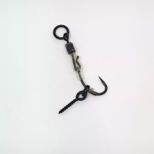 Puede incluir: Un anzuelo de pesca negro con un giratorio y un peso de tornillo. El anzuelo está unido a una línea transparente.