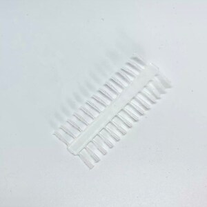 Può includere: Un pettine di plastica bianco con una fila di denti fini. Il pettine è progettato per separare e districare i capelli.