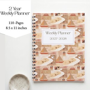 Può includere: Un'agenda settimanale di 2 anni di 21,59 x 27,94 cm con 110 pagine. La copertina presenta un motivo ripetuto di fari, barche a vela e soli in tonalità marrone, beige e arancione. Un'etichetta bianca riporta la scritta Weekly Planner 2027-2028.