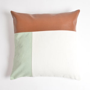 May include: A brown, green and white throw pillow with a geometric design. The pillow is made of a soft, textured fabric.