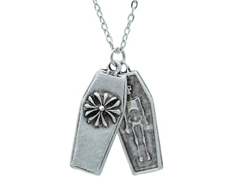 May include: A silver chain necklace with two silver coffin pendants. One pendant features a stylized flower design, while the other features a skeleton.