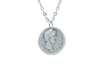 May include: Silver necklace with a round coin pendant featuring a profile of a man with a laurel wreath and the inscription "C.I. CAESAR" on the coin.