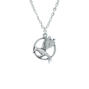 May include: Silver necklace with a pendant featuring a stylized mockingjay bird in flight inside a circle.