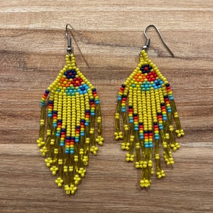 Pu&ograve; includere: Un paio di orecchini di perline gialle con accenti colorati. Gli orecchini sono lunghi e pendenti, con una forma a goccia.