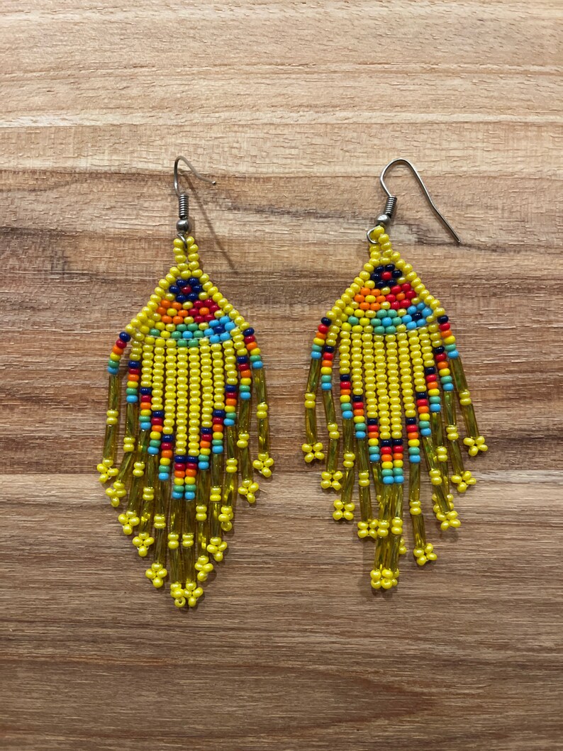 Pu&ograve; includere: Un paio di orecchini di perline gialle con accenti colorati. Gli orecchini sono lunghi e pendenti, con una forma a goccia.