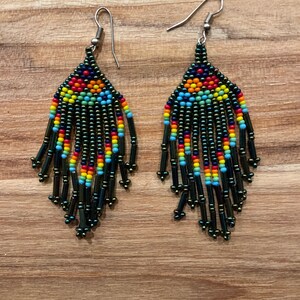 Pu&ograve; includere: Un paio di orecchini pendenti con un design di perline nere, verdi, blu, rosse, gialle e arancioni. Gli orecchini hanno ganci d'argento.