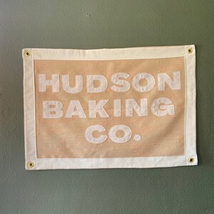 May include: A tan canvas banner with white text that reads "HUDSON BAKING CO."