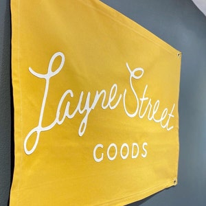 May include: A yellow canvas banner with white text that reads "Layne Street GOODS".