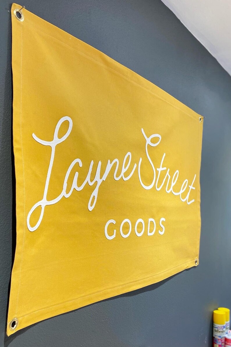 May include: A yellow canvas banner with white text that reads "Layne Street GOODS".