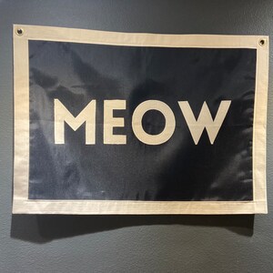 May include: A black and white flag with the word "MEOW" printed in white on a black background. The flag is hanging on a wall.