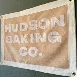 May include: A beige fabric banner with white text that reads "HUDSON BAKING CO."