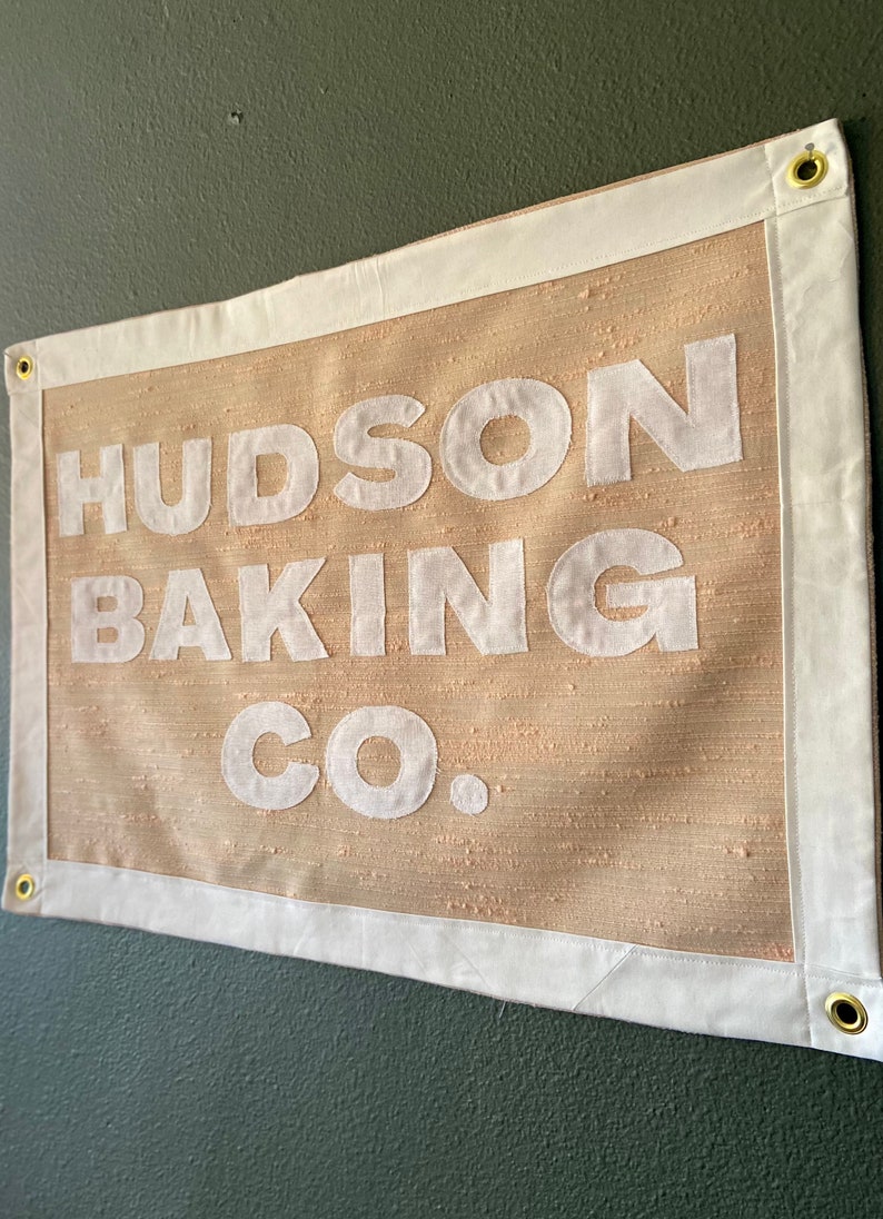 May include: A beige fabric banner with white text that reads "HUDSON BAKING CO."