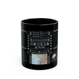 Pode incluir: Caneca de cerâmica preta com um gráfico de um painel de instrumentos de cockpit de aeronave. O painel apresenta uma variedade de botões, interruptores e telas, incluindo uma tela de radar.