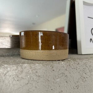 May include: A small, brown and beige ceramic bowl with a speckled glaze.