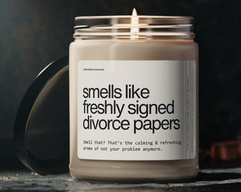 Puede incluir: Una vela beige en un tarro de vidrio transparente con una etiqueta blanca que dice "smells like freshly signed divorce papers. Smell that? That's the calming & refreshing aroma of not your problem anymore."