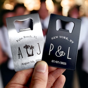 May include: Two rectangular bottle openers, one silver and one black, are held up. The silver opener says "Palm Beach, FL" with "A & J" and a palm tree design. The black opener says "New York, NY" with "P & L" and a heart symbol.