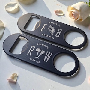 May include: Two matte black flat bottle openers with rounded ends. The top opener features the text NAPLES, FL, the letters F and B, a seashell graphic, and the date 04.18.2026. The bottom opener features DESTIN, FL, R and W, palm trees, and 9-26-26.