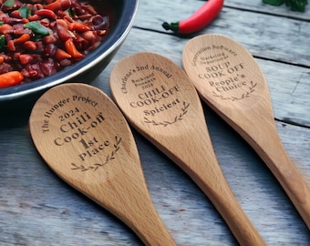 May include: Three light-colored wooden spoons with laser-engraved text. The first reads The Hunger Project 2024 Chili Cook-off 1st Place. The second reads Charlene's 2nd Annual Backyard Bonanza 2024 CHILI COOK-OFF Spiciest. The third reads Generation Software Marketing Department SOUP COOK OFF People's Choice.