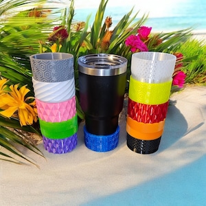 May include: Four different tumblers with colorful, patterned bands. The tumblers are made of stainless steel and have a black, white, gray, and blue color scheme.