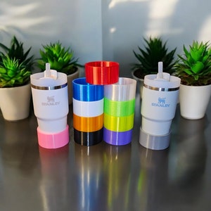 May include: Set of six colorful, stackable, reusable cups with a white, stainless steel travel mug with the word "STANLEY" printed on it.