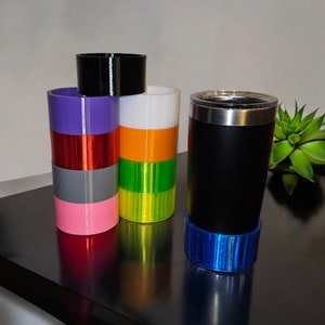 May include: A stack of colorful, cylindrical cups with a black cup on top. A black and silver tumbler with a blue base sits on a black surface.