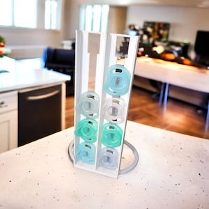 May include: A white plastic stand with six clear and blue pacifiers. The stand has two columns and a base. The pacifiers are arranged in a vertical stack.