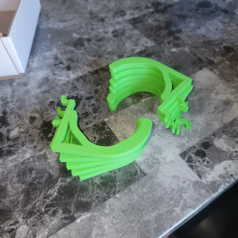 May include: A stack of bright green plastic hooks, likely for hanging items. The hooks are all the same size and shape, and they are arranged in a semi-circle.