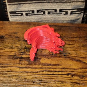 May include: A stack of ten red plastic hooks, likely for hanging items, are arranged in a curved shape on a wooden surface.
