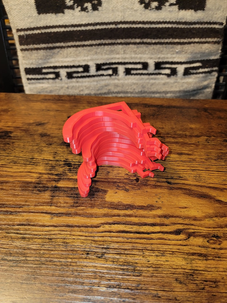 May include: A stack of ten red plastic hooks, likely for hanging items, are arranged in a curved shape on a wooden surface.