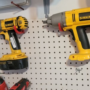 May include: Two yellow DeWalt power tools hanging on a pegboard wall. The tool on the left is a cordless drill with a black battery. The tool on the right is a cordless impact driver with a gray head.