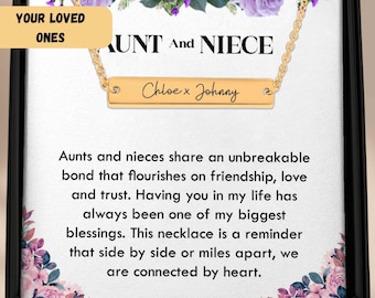 May include: A gold-colored bar necklace with the names "Chloe x Johnny" engraved on it, presented in a black gift box. The box contains a message about the bond between an aunt and niece, with floral accents.