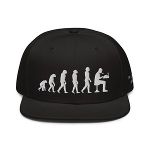 Op de afbeelding: Zwarte baseballpet met een wit geborduurd ontwerp van de evolutie van de mens, eindigend met een persoon die aan een computer zit. De tekst "PROGRAMMER" is aan de zijkant van de pet geborduurd.