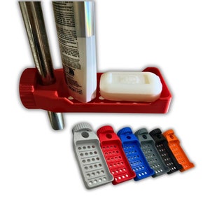 May include: A red plastic soap dish with a bar of soap and a tube of lotion. The dish has a hole for a shower rod and a drain hole. The dish is shown in different colors: gray, red, blue, black, and orange.