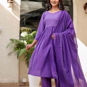 May include: A striking purple salwar kameez outfit. The set features a long-sleeved tunic with detailed embroidery, coordinated straight-leg trousers, and a sheer dupatta. Ideal for celebrations and special events.