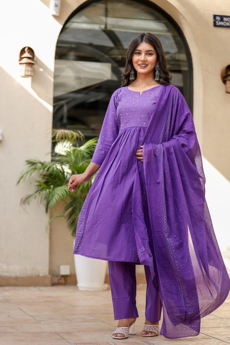 May include: A striking purple salwar kameez outfit. The set features a long-sleeved tunic with detailed embroidery, coordinated straight-leg trousers, and a sheer dupatta. Ideal for celebrations and special events.